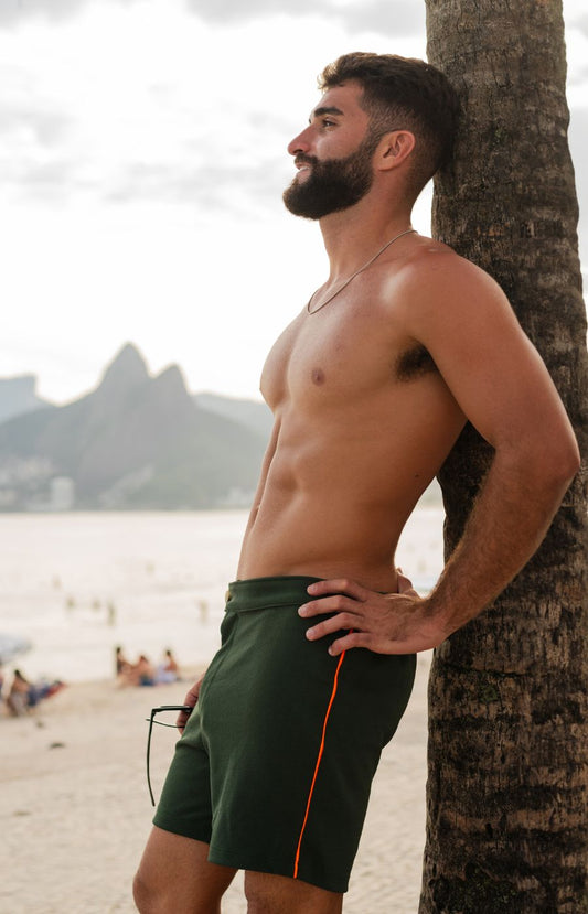 Homem na praia utilizando Short verde militar texturizado com detalhe laranja na lateral